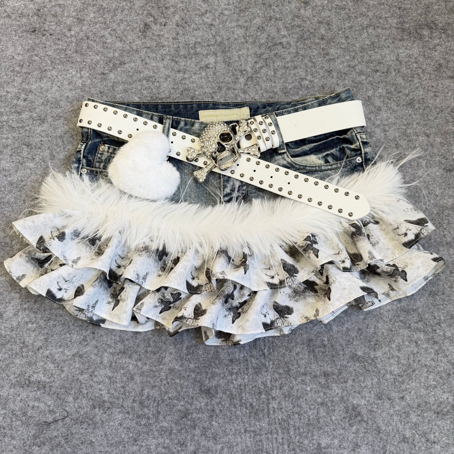 Denim skirt with butterfly-print ruffle layers, wide studded belt and white faux-fur trim