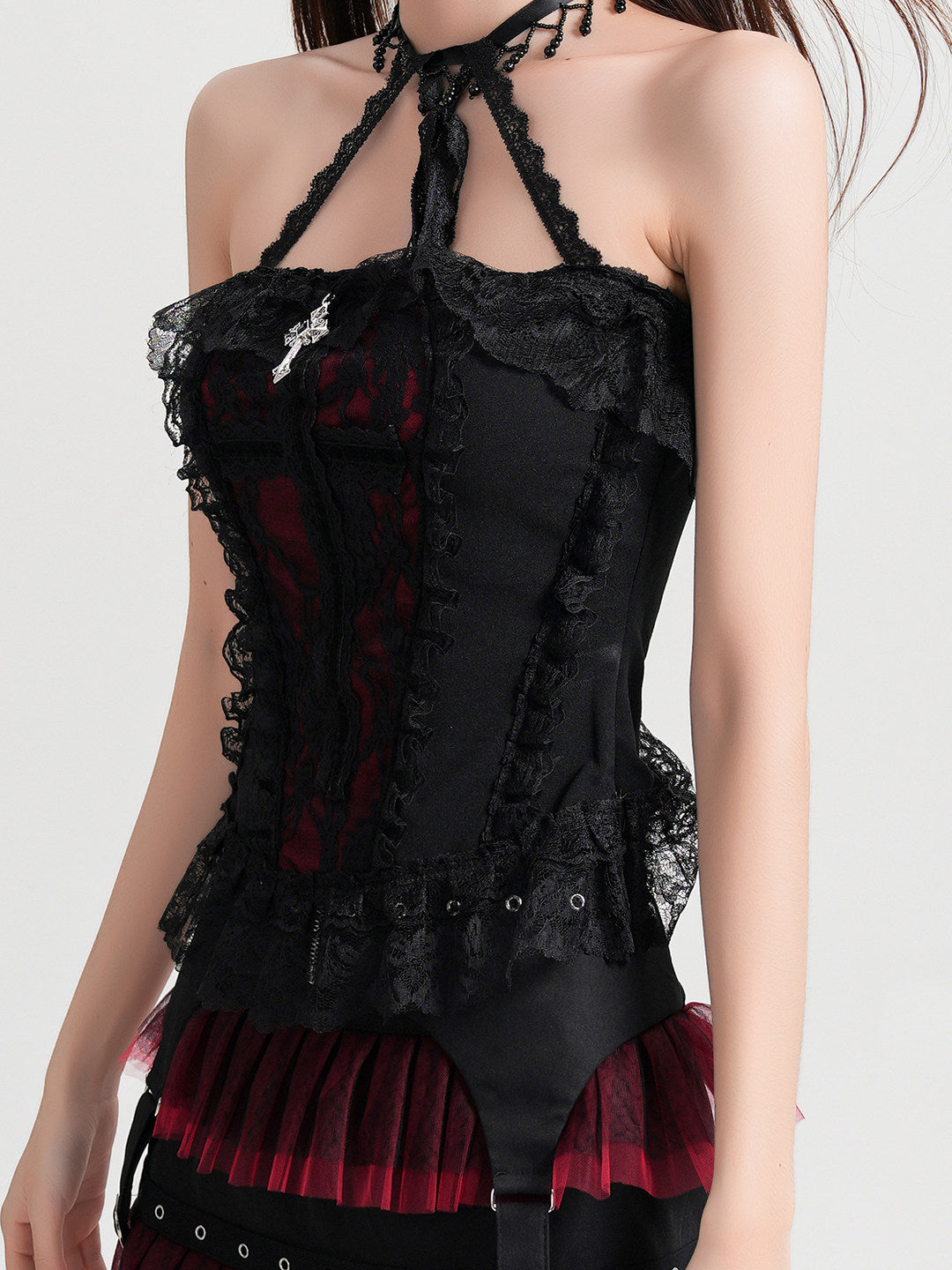 Black lace halterneck vest blouse with crisscross strap back and red pleated ruffle peeking at hem.