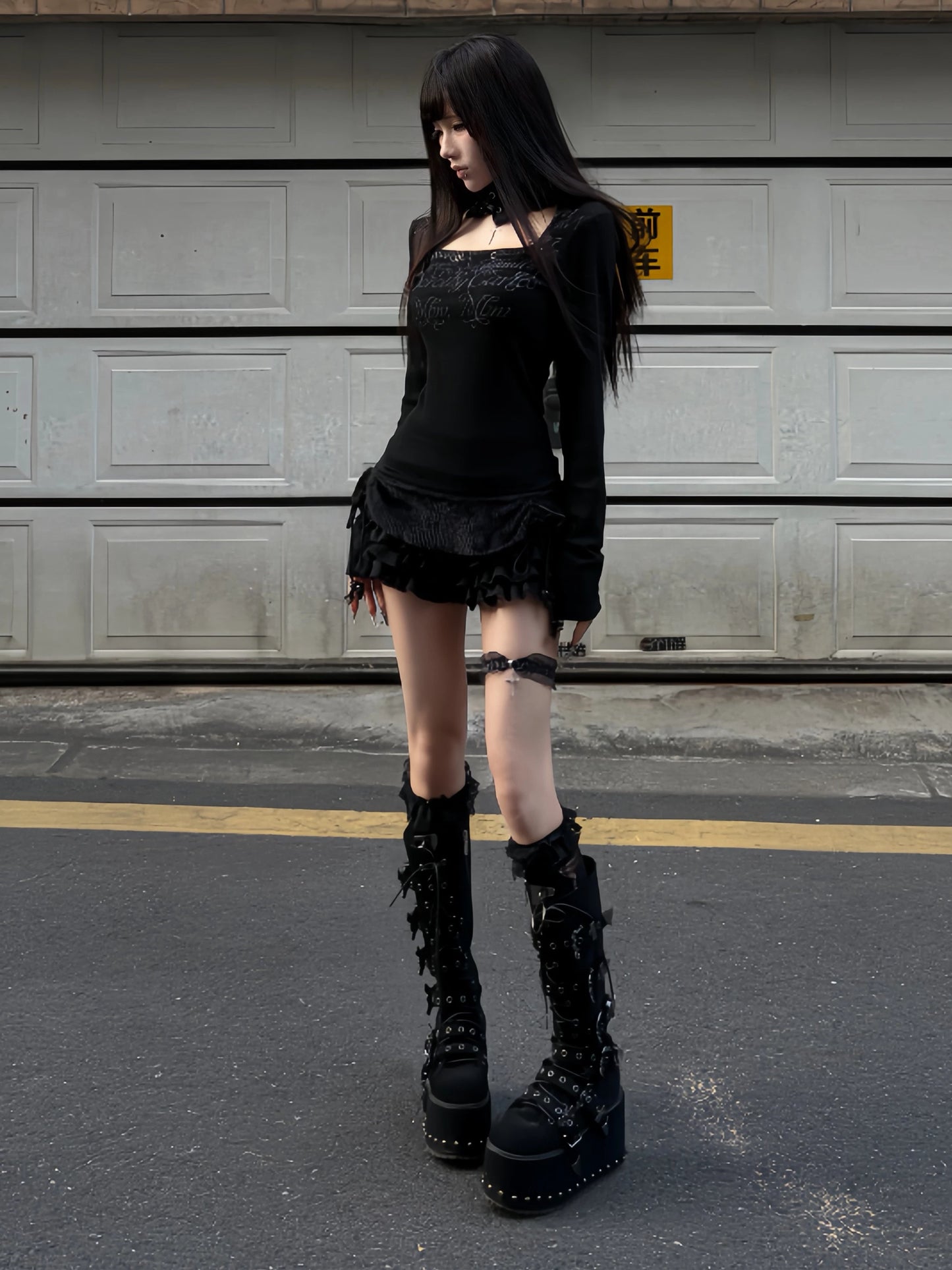 Black long-sleeve top with lace neck loop and script monogram print, ruffled hem