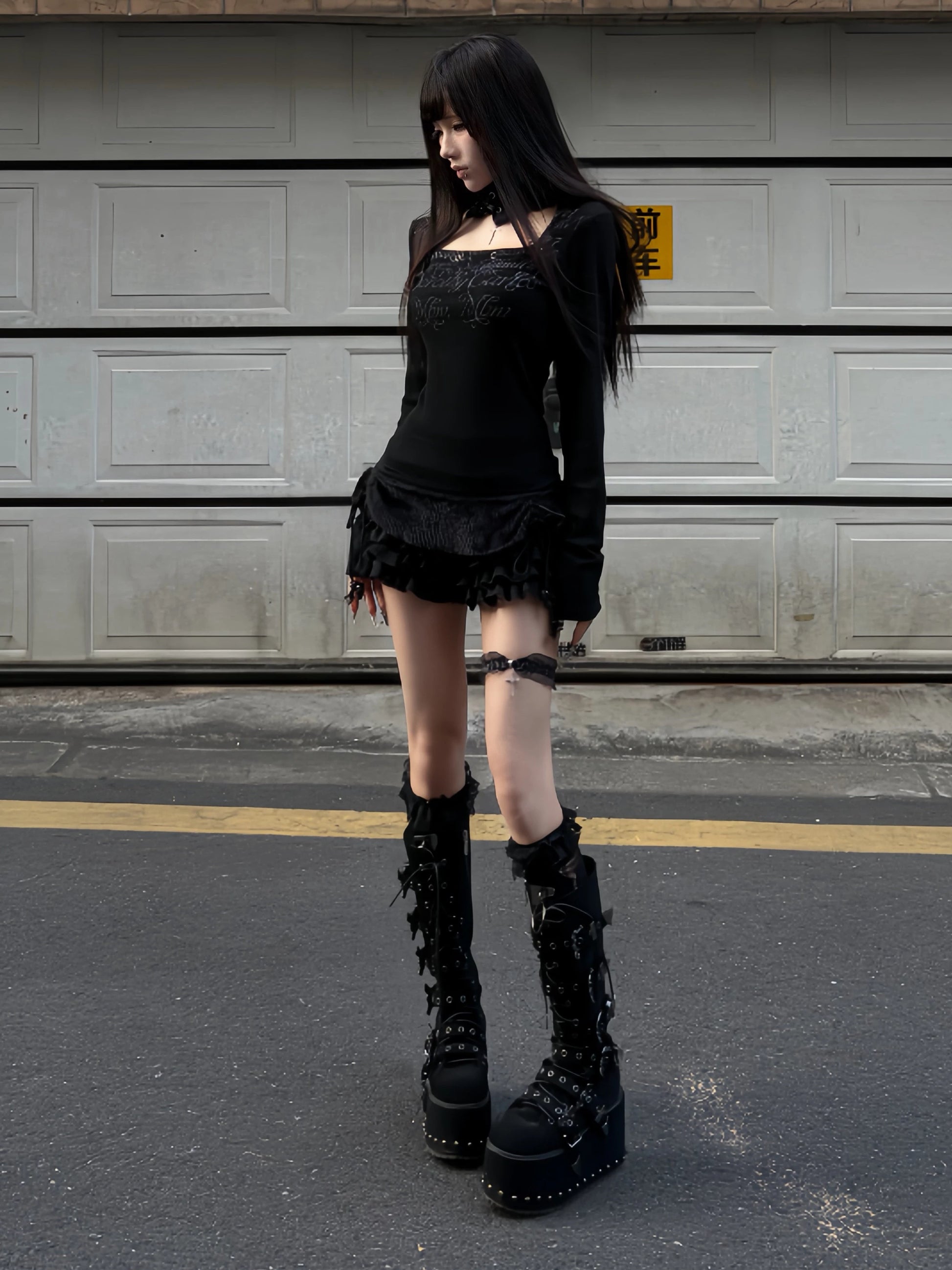 Black long-sleeve top with lace neck loop and script monogram print, ruffled hem