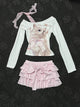 Cream long-sleeve top with cat graphic, lace-trim strap, and layered pink ruffle skirt