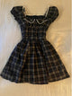 Plaid square-neck dress with puff sleeves, ruffled cream trim, and button bodice; dark plaid.