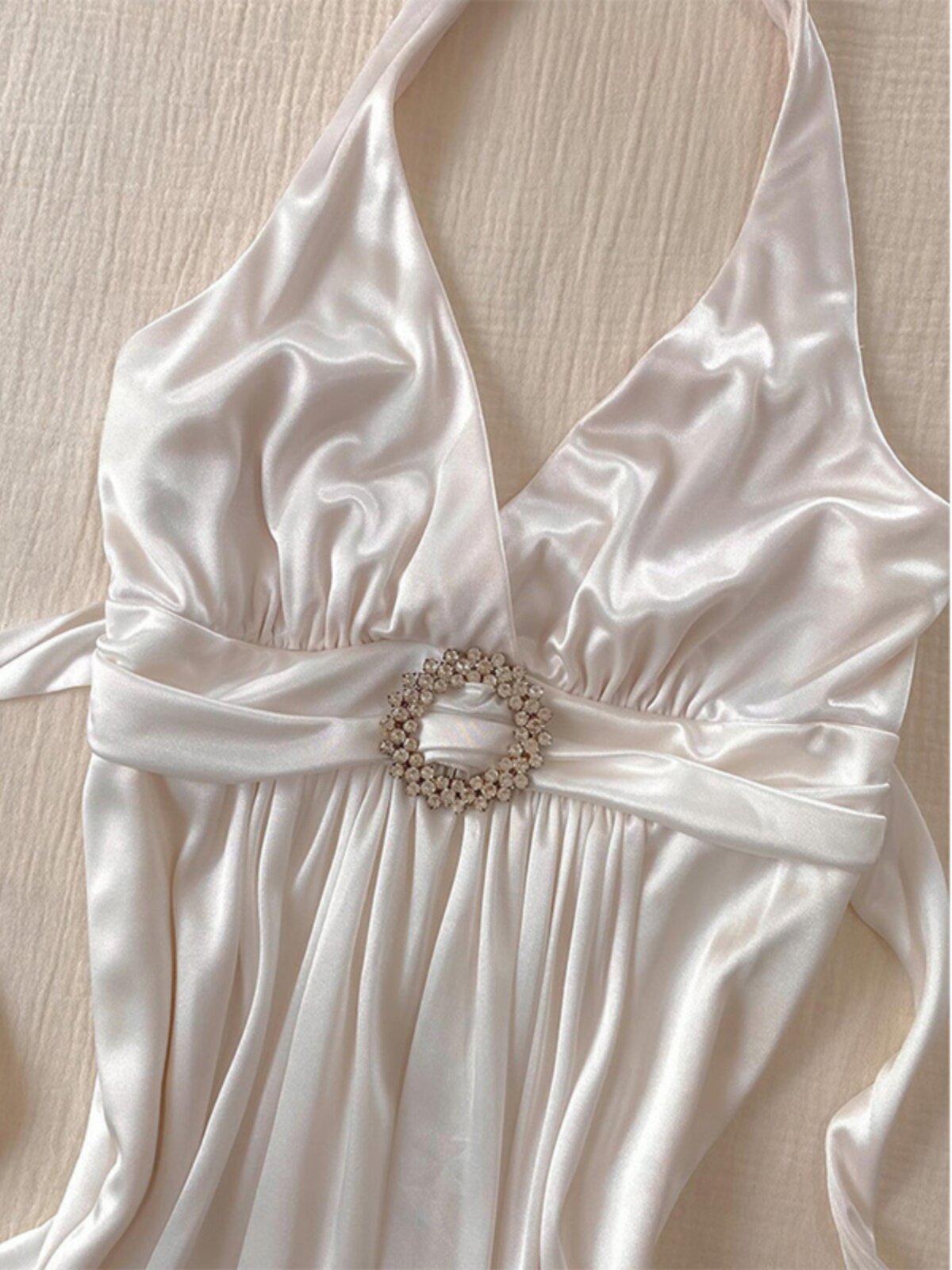 White halterneck slip dress with jeweled belt at waist and draped satin skirt