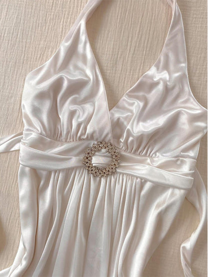 White halterneck slip dress with jeweled belt at waist and draped satin skirt