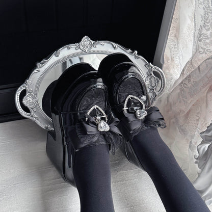 Black platform loafers with ribbon bow and heart charm, glossy finish and lace panels