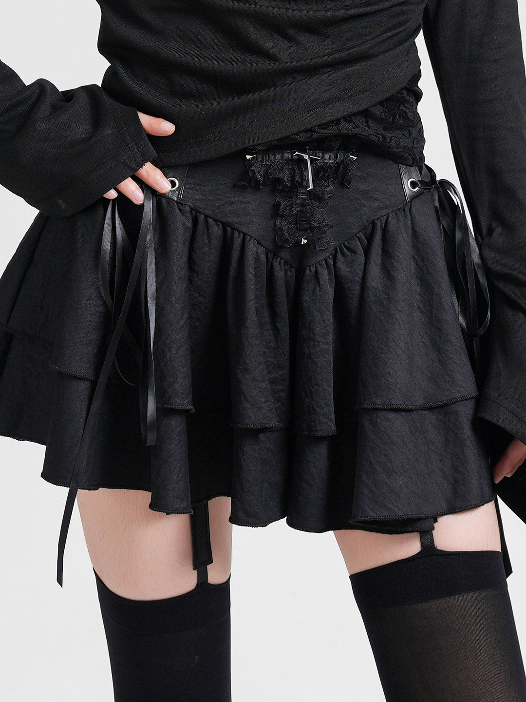 Black layered cake skirt with lace-up waist ties, small studs, and tiered ruffle panels.