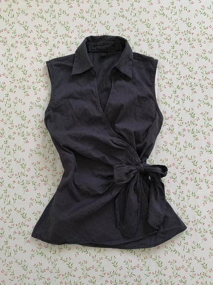 Black sleeveless cardigan top with pointed collar and button front, tied waist bow